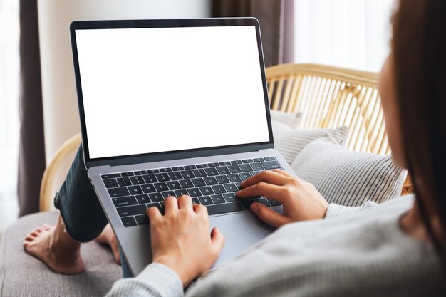 自宅​の​ソファ​に​座っている​間​、​空白​の​画面​で​ラップトップコンピューター​で​作業し​、​入力している​女性​の​モックアップ​画像