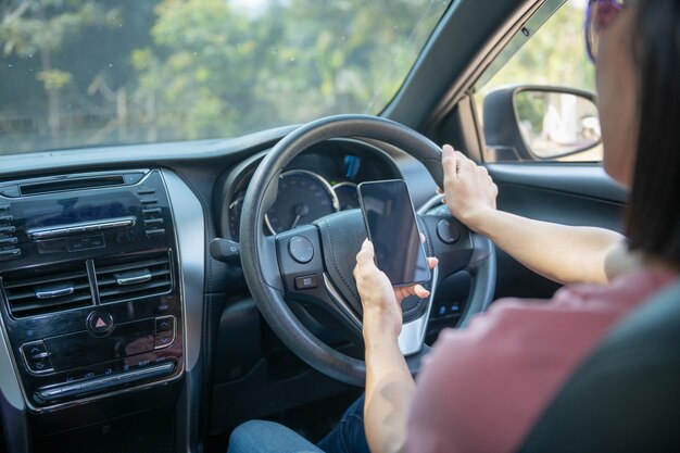 車の運転中に空白の画面で携帯電話を持ち、使用する女性のモックアップ画像、GPS、車内のライフスタイル写真、インテリア、正面図。電話を持つ女性の手で。