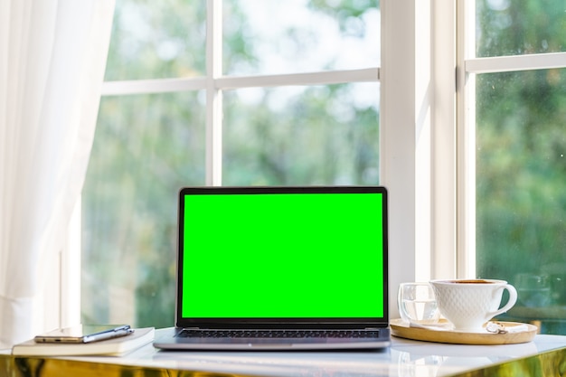 ノート​パソコン​、​コーヒー​カップ​、​テーブル​サイド​に​スマート​フォン​、​カフェ​の​コーヒー​ショップ​の​窓​、​緑​の​画面​と​空​の​画面​の​ラップトップコンピューター​の​モックアップ