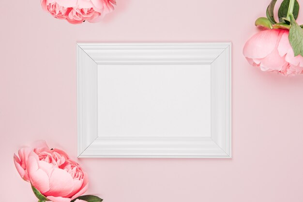 花とピンクの背景にモックアップフォトフレーム。ピンクの牡丹、牡丹のつぼみで繊細でエレガントな背景。フラットレイ、上面図。 Premium写真