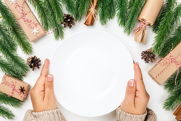 Mockup of white empty plate in hands of woman at christmas holiday dinner concept of family holiday