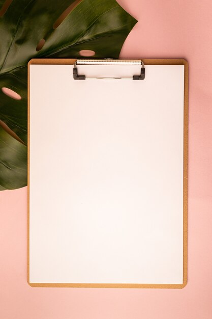 Mockup with clipboard and monstera leaf on pink background. Flat lay, top view, copy space.