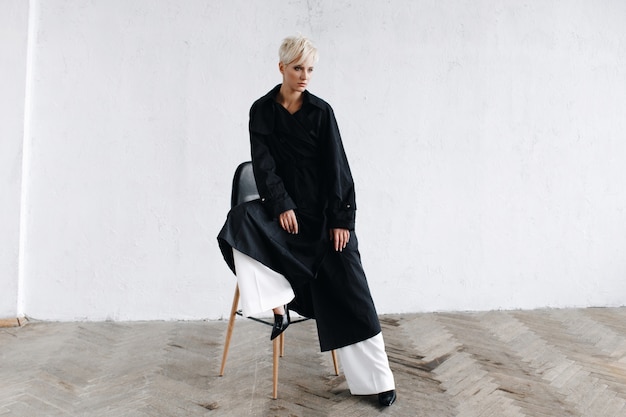 검은 코트에 모델은 사려 깊은 흰 벽 앞에 바 의자에 앉아