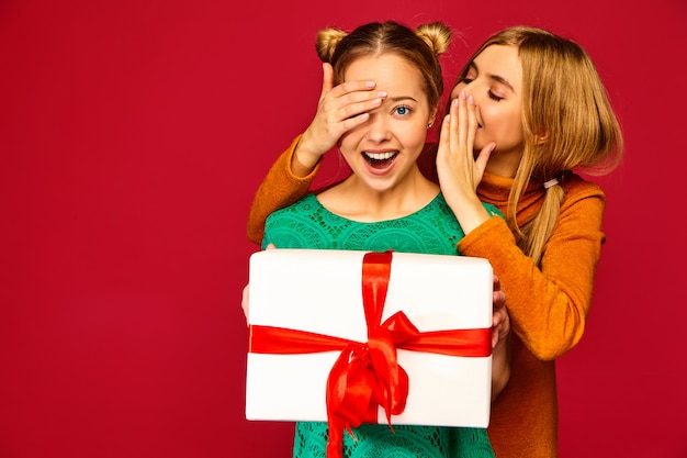 Model covering eyes her friend and giving her big gift box and haring secret