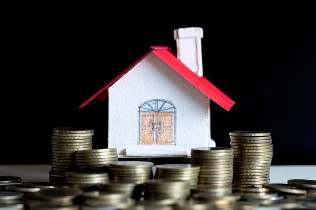 Model of house with coins on wooden table