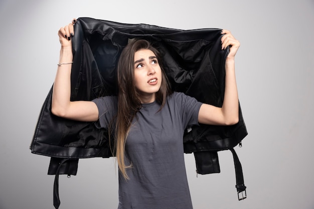 Model looking at her black leather jacket over a gray background.