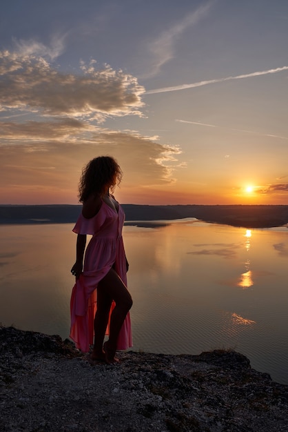 湖の近くの夕日を背景にドレスを着てポーズをとるモデル