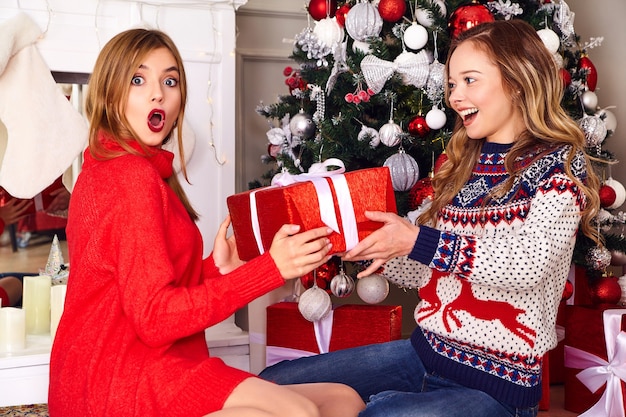 Models in warm winter sweaters sitting near decorated Christmas tree at New Year eve.