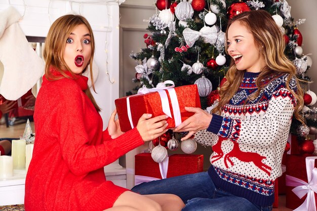 Models in warm winter sweaters sitting near decorated Christmas tree at New Year eve.