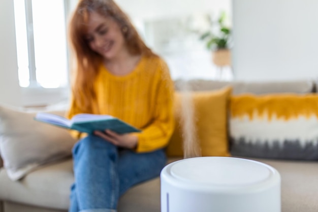 Modern air humidifier and blurred woman resting reading a book on sofa on background