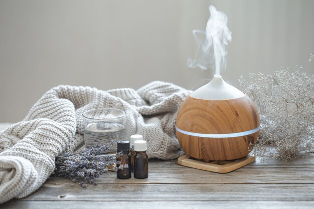 Modern aroma oil diffuser on wood surface with knitted element, water and oils in jars.