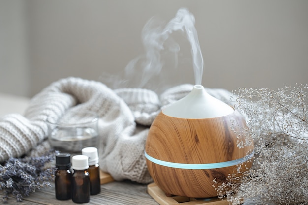 Free photo modern aroma oil diffuser on wood surface with knitted element, water and oils in jars.