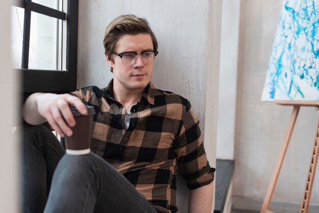 Modern artist looking at his painting while holding a cup of coffee