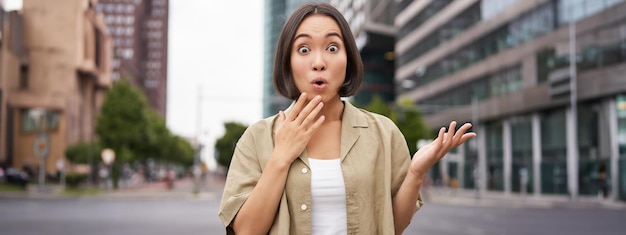 Foto gratuita ragazza asiatica moderna in piedi sulla strada con la faccia sorpresa che sembra impressionata e stupita, sente fantastico