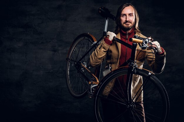 Modern bearded hipster in red sweater is holding his bike while posing for photographer.