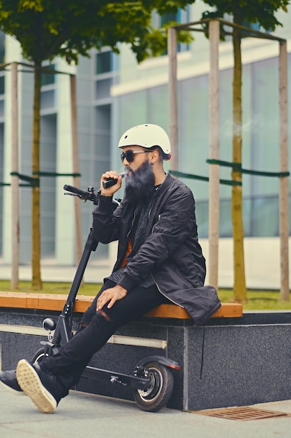 Modern bearded male vaping after electric scooter.