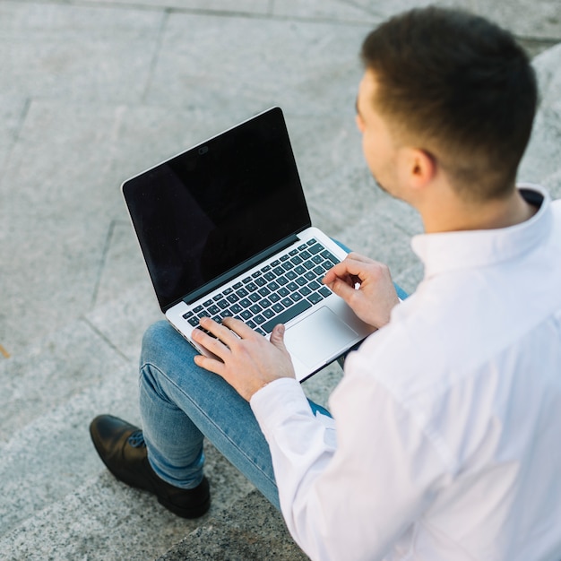 Uomo d'affari moderno che per mezzo del computer portatile all'aperto