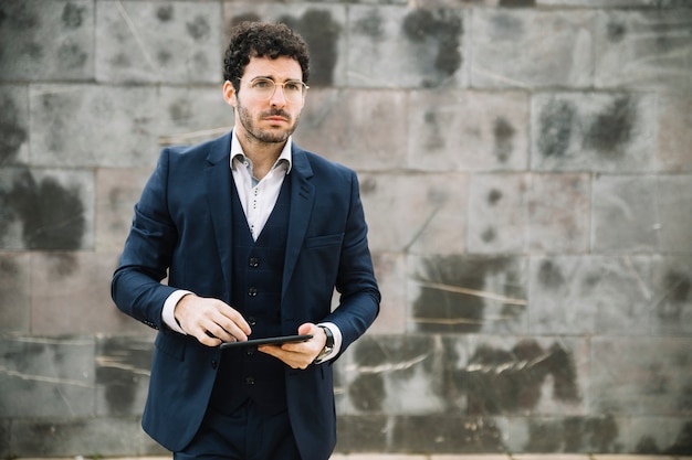 Modern businessman using tablet in front of wall