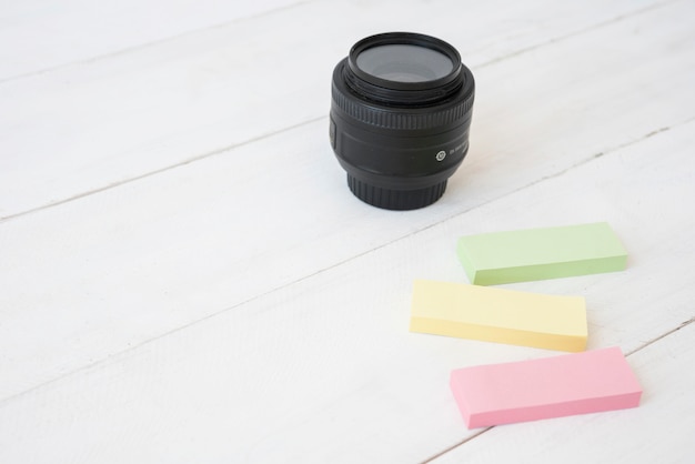 Modern camera lens with colorful sticky notes on wooden desk