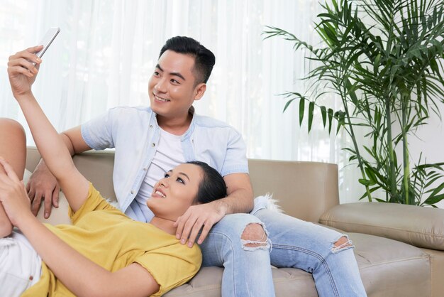 Modern couple taking selfie on couch at home