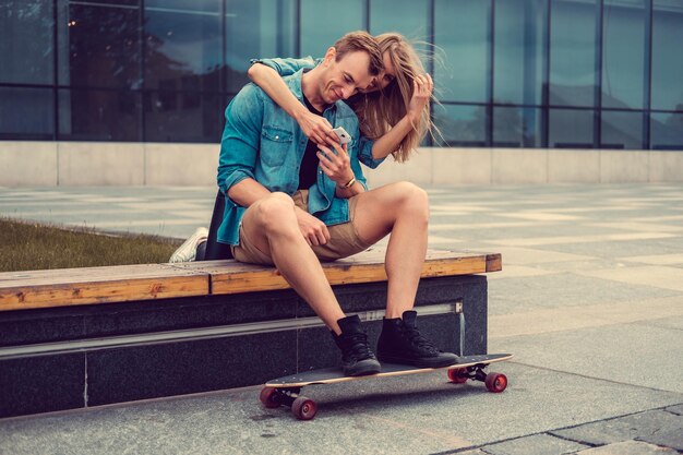 Modern couple using smartphone after longboard ride in a city.