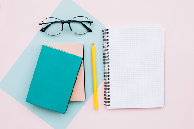 modern desktop with glasses and books and notebook on pastel colors background