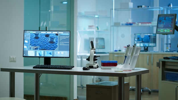 Modern empty biological applied science laboratory with technological microscopes, glass test tubes, micropipettes, desktop computers and displays. PC's are running sophisticated DNA calculations.