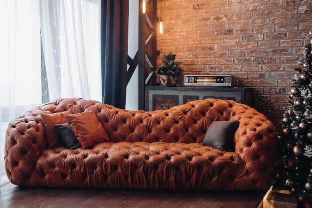 Modern fashionable red leather couch with cushions. Cropped Christmas tree. Brick wall. Loft design.