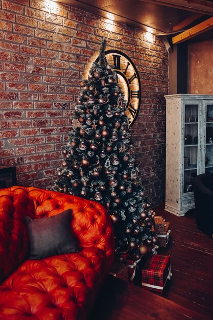 Modern fashionable red leather couch with cushions. Cropped Christmas tree. Brick wall. Loft design.