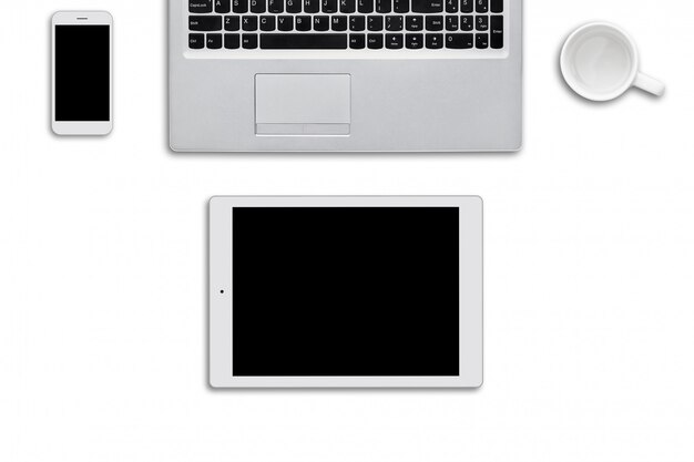 Современные гаджеты, лежащие на белой поверхности. Портативный компьютер, планшет и смартфон и белая пустая чашка на белой стене. Вид сверху современных устройств, которые необходимы для серфинга в Интернете или работы. Технологии
