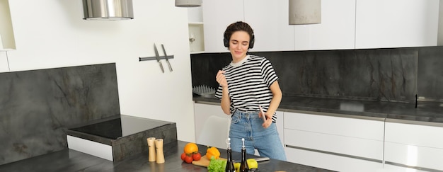 Free photo modern happy woman dancing and cooking listening music in headphones making a vegan healthy meal