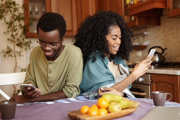 Modern internet addicted young African American couple using electronic gadgets during breakfast