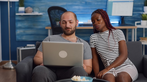 Modern interracial couple using laptop on couch at home