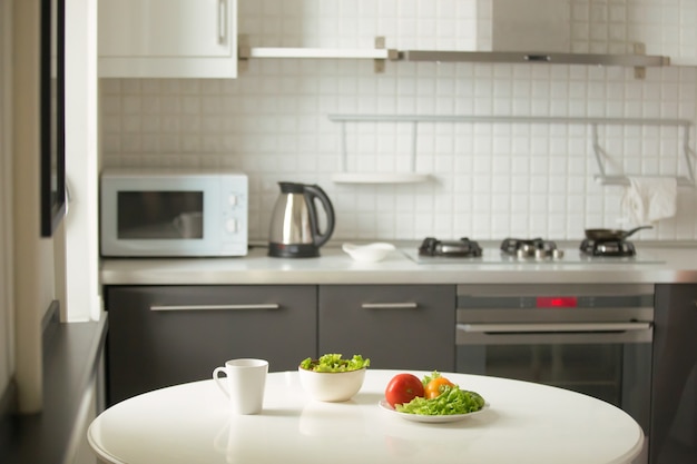 Modern kitchen, a white table, mug and green salad Free Photo