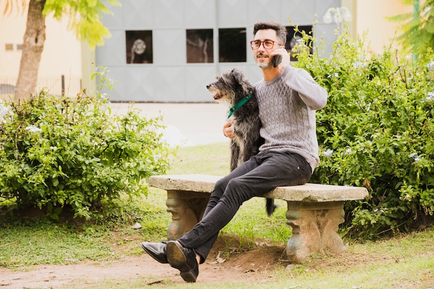 彼の犬が携帯電話で話していると公園に座っている現代人