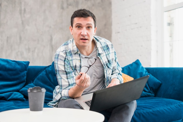 Free photo modern man sitting on sofa and surfing on laptop at home