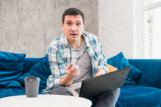 Modern man sitting on sofa and surfing on laptop at home