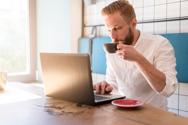 Современный человек, работающий на своем ноутбуке, попивая кофе