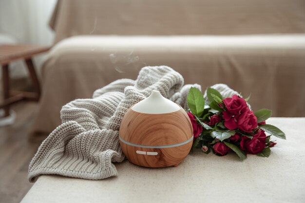 Modern oil aroma diffuser in the living room on the table with knitted element and flowers.