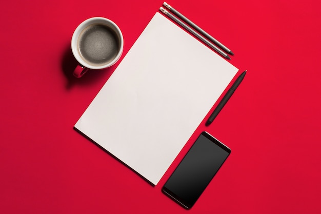 スマートフォンと一杯のコーヒーでモダンな赤いオフィスデスクテーブル。