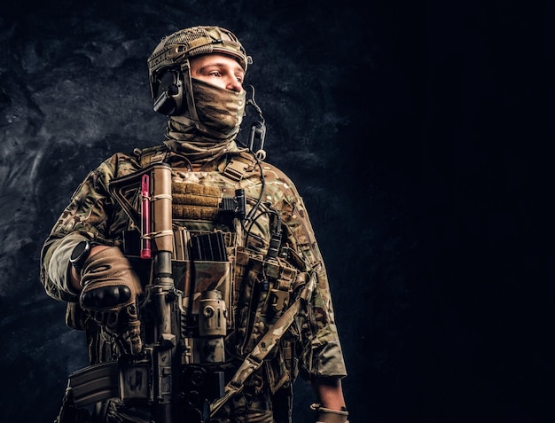 Free photo modern special forces soldier in camouflage uniform looking sideways. studio photo against a dark textured wall.