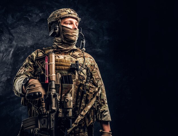 横向きのカモフラージュ制服を着た現代の特殊部隊の兵士。暗いテクスチャの壁に対するスタジオ写真。