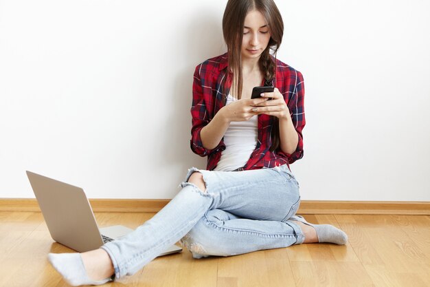 Modern stylish girl dressed in checkered shirt and ragged jeans relaxing at home