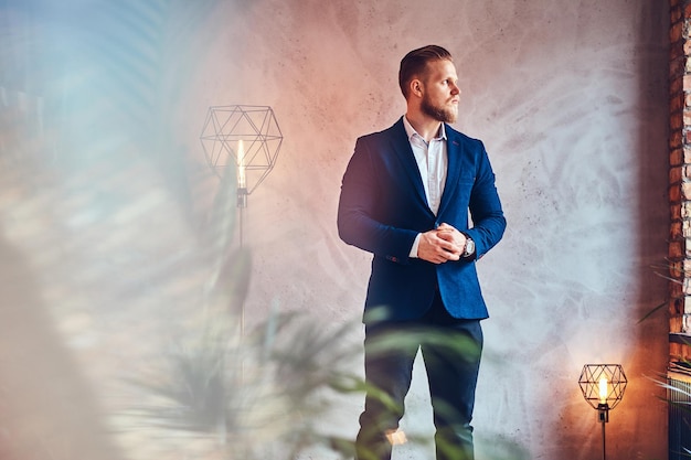 Free photo a modern, stylish male dressed in an elegant suit posing in a room with loft interior.