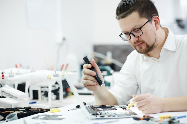 Foto gratuita tecnico moderno inspecting laptop con torcia