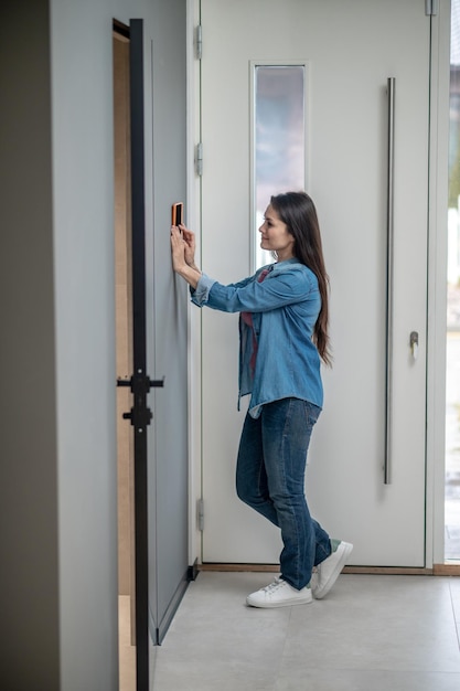Modern technologies Young adult woman standing sideways to camera near smart home device
