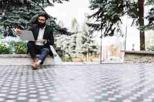 Free photo modern young businessman sitting in the park looking at laptop