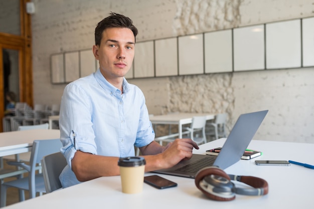 Free photo modern young handsome man sitting in open space office working on laptop