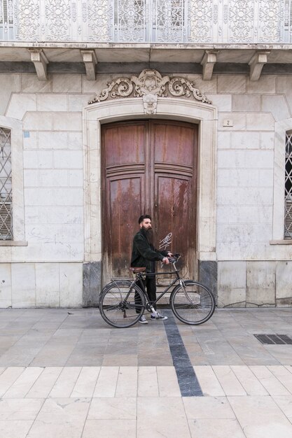 閉じたドアの前に彼の自転車の地位を持つ現代の若い男