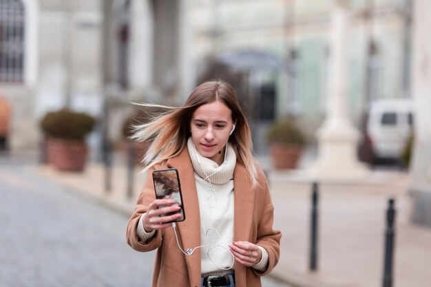 Modern young woman listening to music on earphones outside